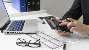 Mãos mexendo em computador e calculadora sob a mesa