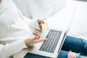 Mulher segurando cartão em frente ao notebook