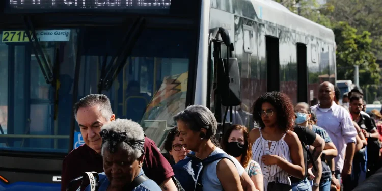 Águia Branca anuncia 75 vagas de empregos para diversos cargos 1 Passageiros descendo de ônibus lotado em um ponto de transporte público movimentado durante o dia.