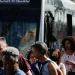 Passageiros descendo de ônibus lotado em um ponto de transporte público movimentado durante o dia.