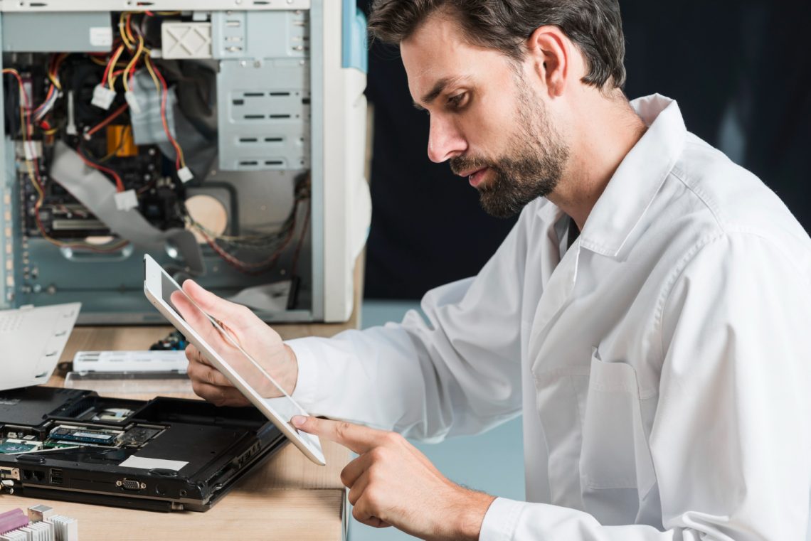 Técnico de informática analisando um tablet enquanto trabalha na manutenção de computadores