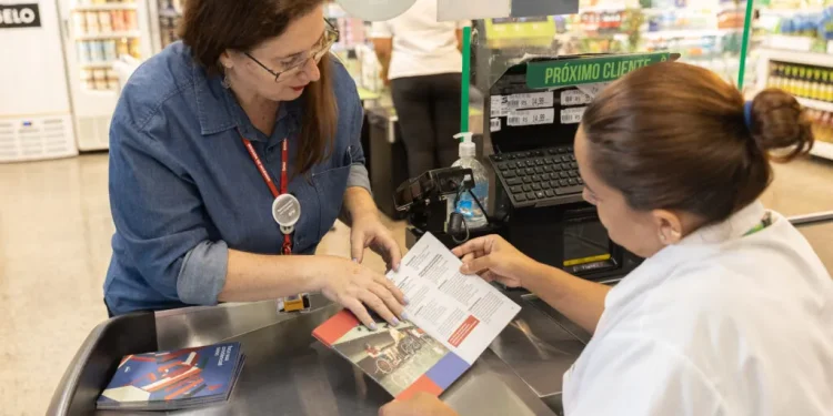  Funcionária orientando cliente no caixa de supermercado com material informativo.