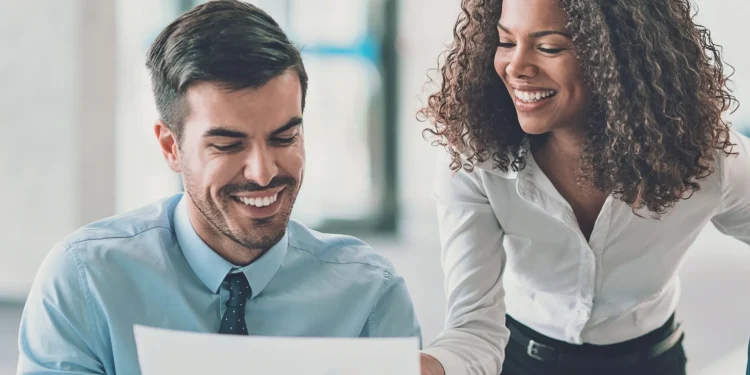 Colegas de trabalho sorrindo enquanto analisam um documento no escritório.