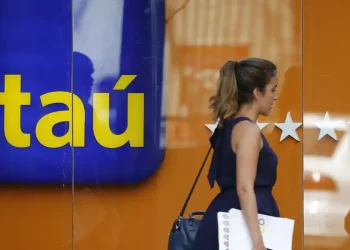 Mulher passando em frente ao banco Itaú, com o logo visível.