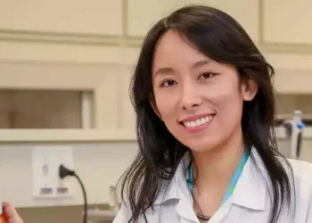 Cientista sorrindo ao lado de equipamento de laboratório.