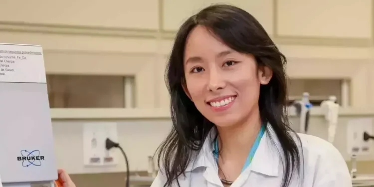Cientista sorrindo ao lado de equipamento de laboratório.
