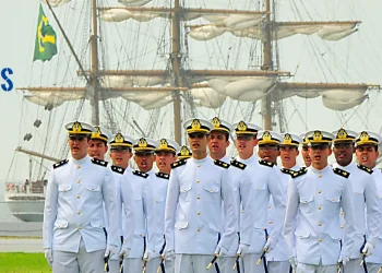 Oficiais da Marinha do Brasil em desfile com navio ao fundo.