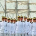 Oficiais da Marinha do Brasil em desfile com navio ao fundo.