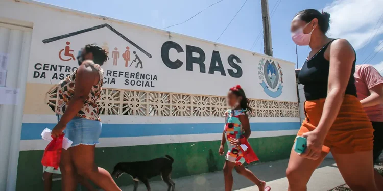Pessoas caminhando em frente a um centro do CRAS em dia ensolarado.