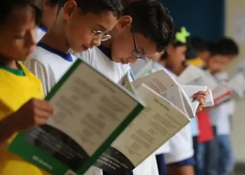 Crianças em fila lendo livros na escola.