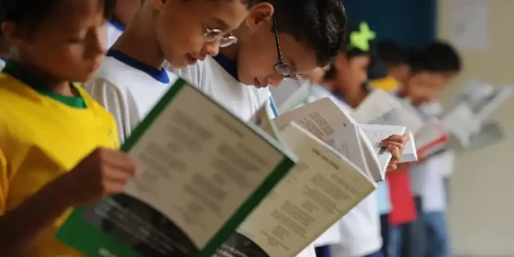 Crianças em fila lendo livros na escola.