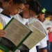 Crianças em fila lendo livros na escola.
