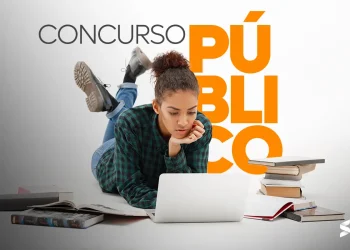 Jovem estudando para concurso público com um notebook, cercada por livros e anotações.