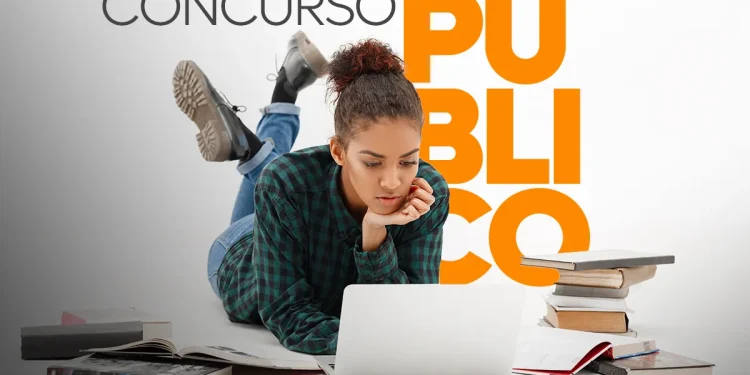 Jovem estudando para concurso público com um notebook, cercada por livros e anotações.