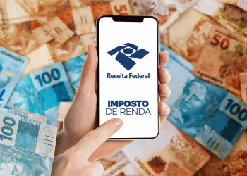 Pessoa acessa o sistema do Imposto de Renda no celular com fundo de cédulas de real.