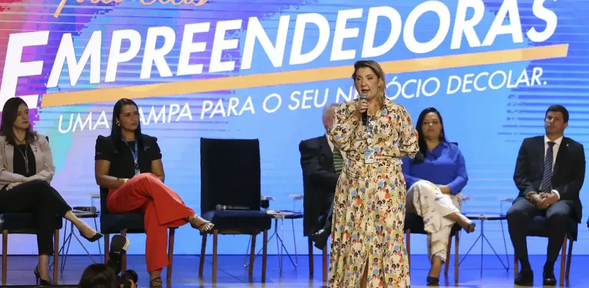 "Mulher palestrante em evento de empreendedorismo, com painel 'Caixa pra Elas' ao fundo, destacando a importância do marketing e posicionamento de marca.