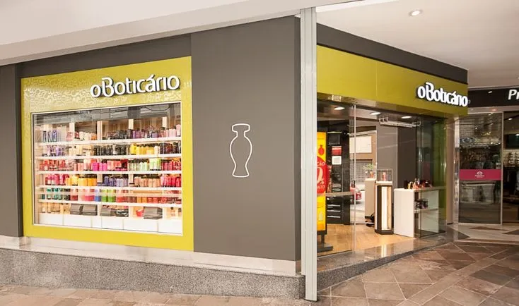  Fachada de uma loja do Boticário em um shopping, exibindo produtos de perfumaria e cosméticos.