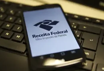 Smartphone exibindo o aplicativo da Receita Federal sobre um teclado de computador.