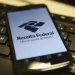 Smartphone exibindo o aplicativo da Receita Federal sobre um teclado de computador.