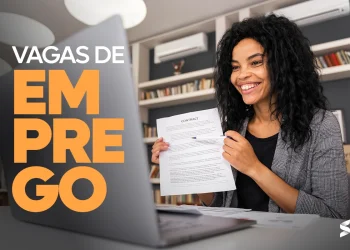 "Mulher sorrindo enquanto segura documentos em frente a um laptop, ilustrando uma vaga de emprego home office na C&A."