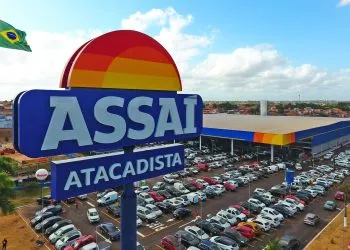 Fachada do Assaí Atacadista com estacionamento cheio e bandeira do Brasil ao fundo