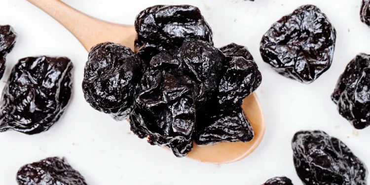 Ameixas secas em colher de madeira sobre fundo branco – alimento rico em fibras e antioxidantes.