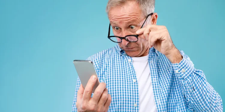 Homem mais velho ajustando os óculos enquanto observa um smartphone com expressão de curiosidade.