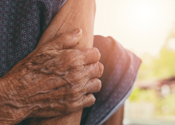 Mãos envelhecidas segurando o braço, simbolizando a importância da aposentadoria para idosos.