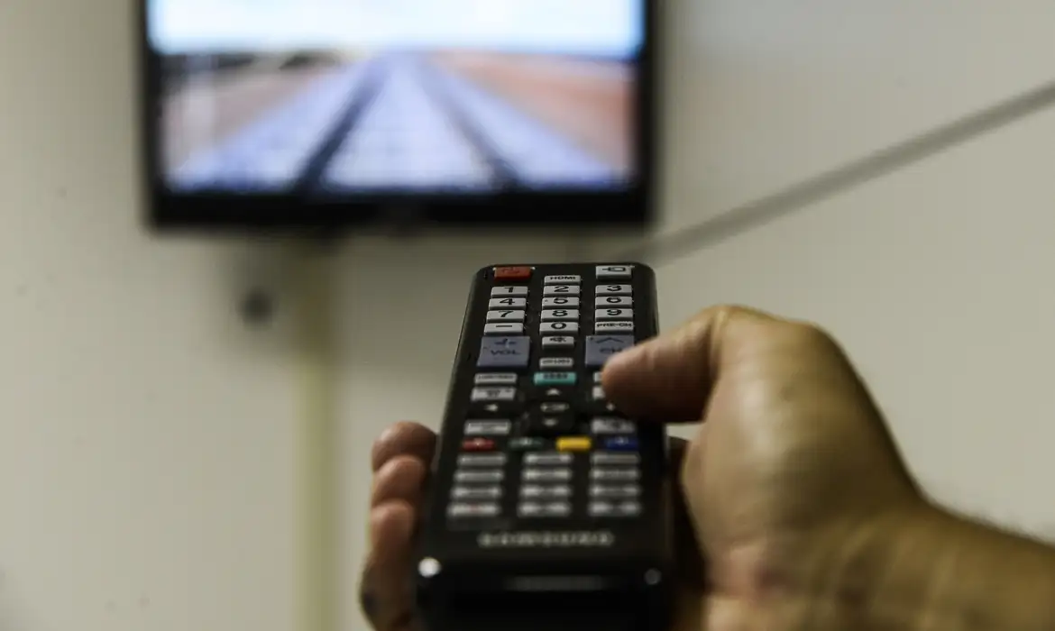Pessoa segurando controle remoto apontando para TV.
