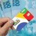 Cartão do programa social Bolsa Família 2025 sendo segurado por uma mão, com cédulas de dinheiro ao fundo.