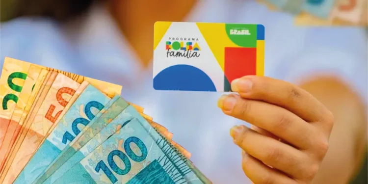Cartão do Bolsa Família sendo segurado com cédulas de dinheiro ao fundo