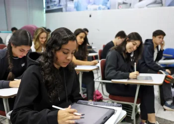 Estudantes concentrados em sala de aula, utilizando cadernos e tablets.