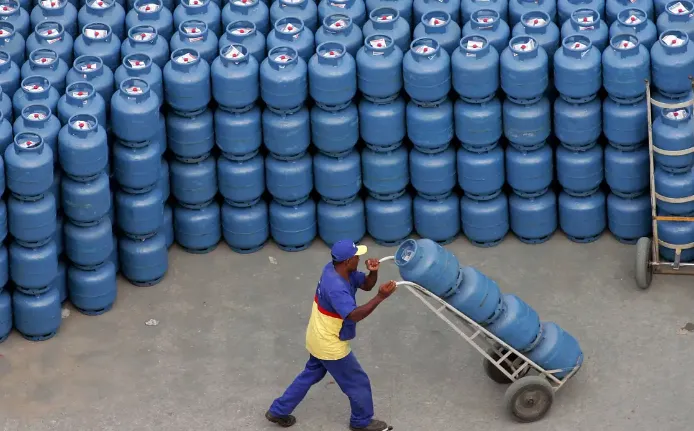 Trabalhador transportando botijões de gás azul empilhados, simbolizando a entrega do Auxílio Gás.