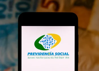 Logo da Previdência Social exibido na tela de um smartphone, com notas de dinheiro ao fundo, relacionado ao tema de verificação de descontos indevidos no INSS.