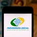 Desconto indevido no INSS? Saiba como verificar e recuperar os valores 8 Logo da Previdência Social exibido na tela de um smartphone, com notas de dinheiro ao fundo, relacionado ao tema de verificação de descontos indevidos no INSS.