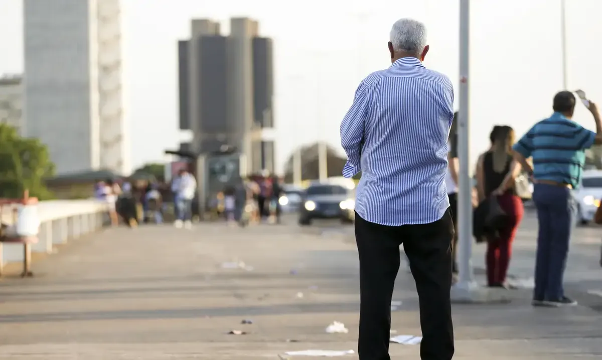 Homem idoso de costas em rua movimentada, representando a população afetada pelas novas regras de aposentadoria do INSS em 2025.