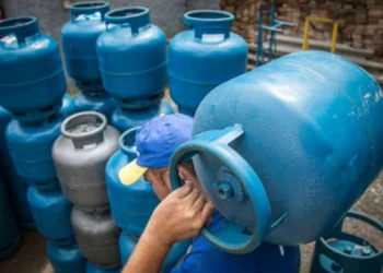 Trabalhador carregando botijão de gás azul em estoque, representando a distribuição do Auxílio Gás.