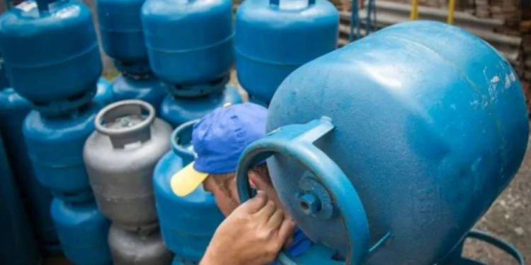 Trabalhador carregando botijão de gás azul em estoque, representando a distribuição do Auxílio Gás.