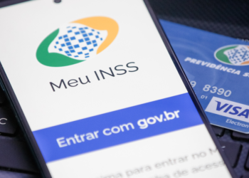 Aplicativo Meu INSS exibido em celular ao lado de cartão de benefício da Previdência Social.