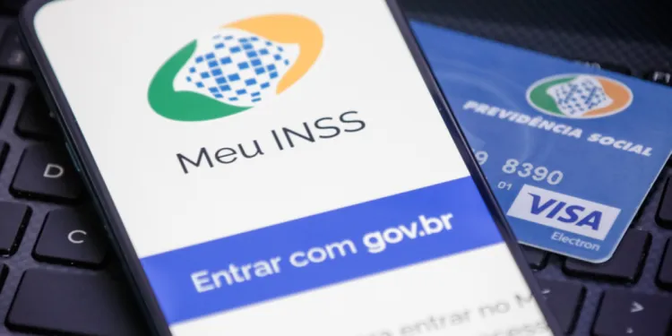 Aplicativo Meu INSS exibido em celular ao lado de cartão de benefício da Previdência Social.
