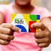Cartão do Programa Bolsa Família sendo segurado por uma criança, com cores vibrantes e logo visível.