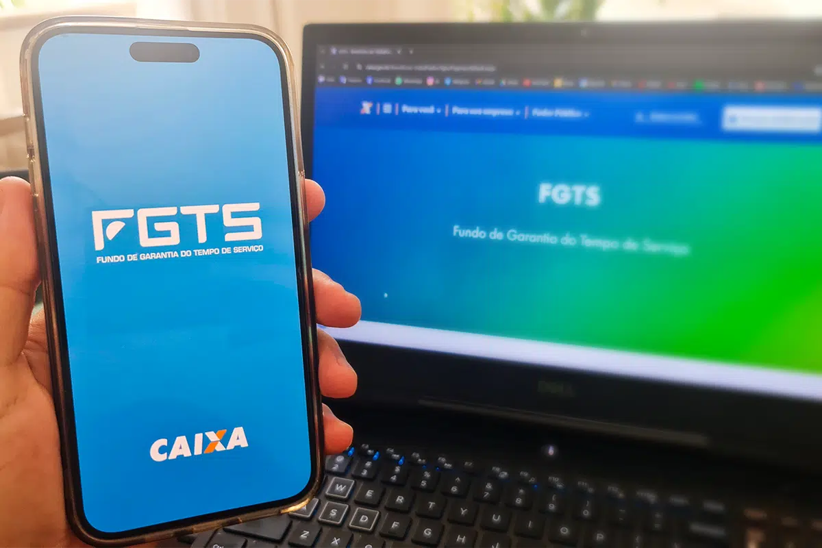 Tela de celular com logo do FGTS e site da Caixa no computador