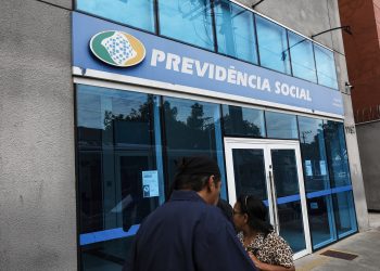 Agência do INSS mostrando o logo da Previdência Social e pessoas nas proximidades
