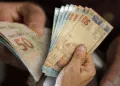 Cédulas de reais sendo manuseadas por mãos idosas, simbolizando o recebimento de benefícios sociais