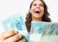 Mulher sorrindo com notas de 100 reais, representando apoio financeiro do programa Mães de Pernambuco 2025