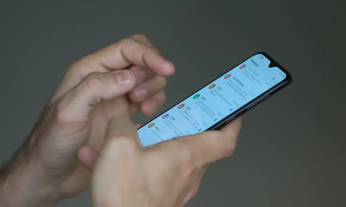 Pessoa utilizando smartphone para ilustrar golpes aplicados por falsos agentes do SUAS.