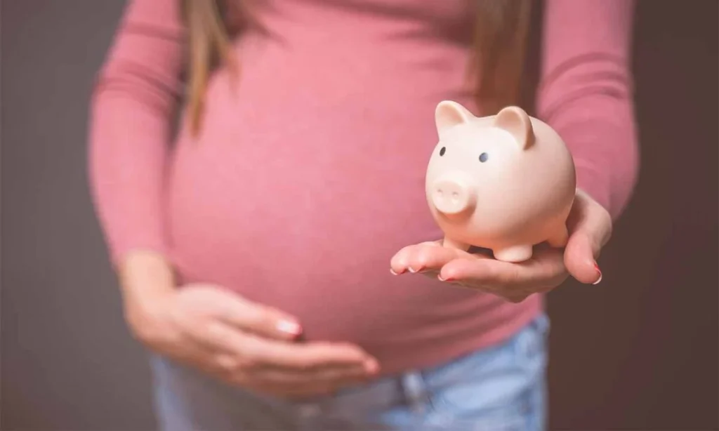 jovem gravida segura a sua barriga enquanto carrega um cofrinho rosa em formato de porquinho.