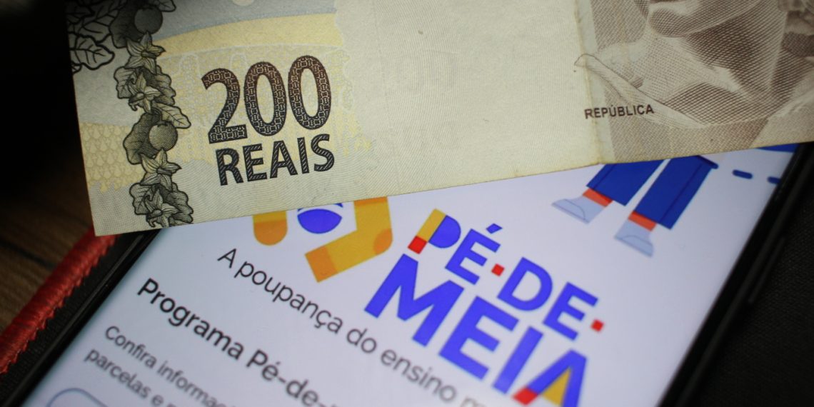 Nota de R$ 200 sobre um celular com a tela mostrando o logo do programa Pé-de-Meia, destacando o benefício do programa.