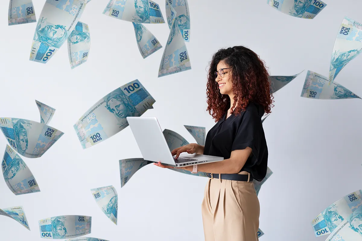  Mulher sorridente usando laptop com cédulas de 100 reais flutuando ao redor