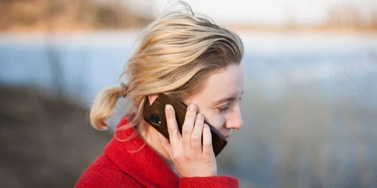 Jovem mulher loira, em área externa, falando ao celular, simbolizando a necessidade contínua de fazer ligações interurbanas e entender o código DDD, para ligar para outro estado.